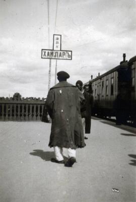 Man walking on the Trans-Siberian Railway platform by the train in Harbin, China; written in pencil on the back: China.