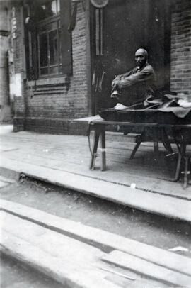 Man sitting on a table at a bazaar in Fushun, Manchuria in northern China; written in pencil on the back: Futachien 1924.
