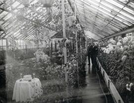 Dr. N.E. Hansen and an another man are in a greenhouse full of flowers on the campus of South Dakota State College.