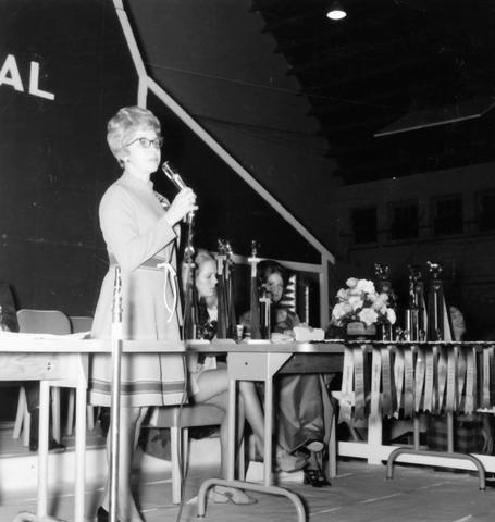Women speaking into a microphone stands behind a table with trophies at the Little International Agricultural Exposition at South Dakota State University.