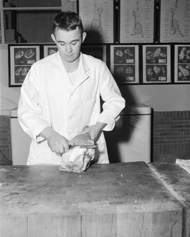 Man cutting meat during the meat judging competition at the 1956 Little International Exposition at South Dakota State College.