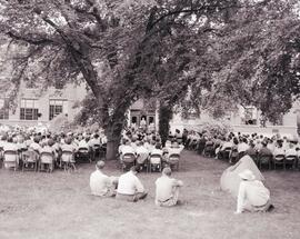 People seated in folding chairs and the grass in front of Lincoln Memorial Library on the campus of South Dakota State College to hear Carl Hansen speak during the recognition service for Dr. N.E. Hansen for his work in horticulture.