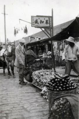 N.E. Hansen looking at onions and other vegetables for sale at a bazaar in Fushun, Manchuria in northern China; written in pencil on the back: Onions, etc. at Futachien 1924.