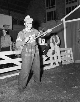 Clown holding a rake like a guitar and pretending to play at the 1963 Little International Exposition at South Dakota State College.