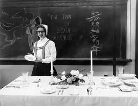 Woman standing by a set dinner table in the Home Economics exhibit at the 1959 Little International Exposition at South Dakota State College. She is wearing a traditional Scandinavian folk costume.
