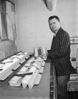 Vernon Voss, winner of the poultry contest, is holding a carton of eggs at the poultry exhibit at the 1960 Little International Exposition at South Dakota State College. There are many other cartons of eggs on the table in front of him.