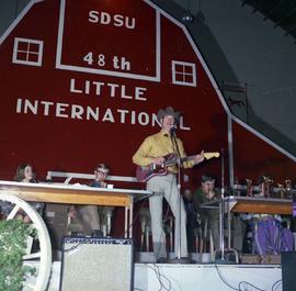 Man plays a guitar and sings into the microphone on the stage at the 1971 Little International exposition at South Dakota State University.