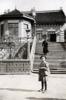 Man walking down the stairs at the railway station in Saolin in northern China, a young girl is standing at the foot of the stairs; written in pencil on the back: Railway station Saolin North China 1924.