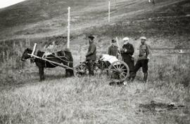 N.E. Hansen and his three assistants gathering specimens in a field with a horse-drawn wagon at Mendoche before they begin a search for hardy peach trees in northern China, there is a dog in the grass; written in pencil on the back: Mendoche 1924 North China.