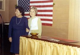 Millie Denholm at an event. She is standing with a woman in front of a U.S. flag.