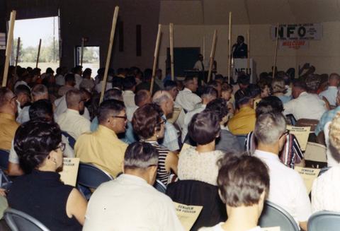 Frank Denholm at a podium in the back of the room at a National Farmers Organization in Miller, South Dakota