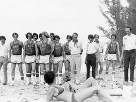 South Dakota basketball delegation to Cuba players in USA team uniforms standing on Cuban beach with two women subathing in the foreground