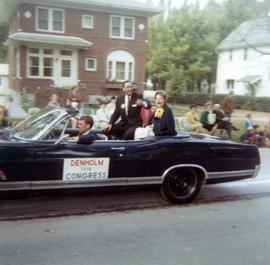 Frank Denholm and his wife, Millie, are in a parade riding in the back of a convertible.