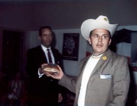 Frank Denholm is handing a man wearing a cowboy hat a sandwich at a campaign event.