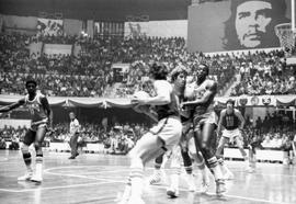 Action photo of basketball game between USA team from South Dakota delegation and Cuban national team in Cuba. A mural of Ernesto Che Guevara and scoreboard showing score of 22 South Dakota and 36 Cuba are in background.
