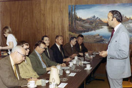 Frank Denholm in a restaurant talking to a group of men.