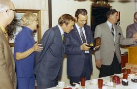 Frank Denholm and another man are looking at a gold watch gifted to Denholm at an event.