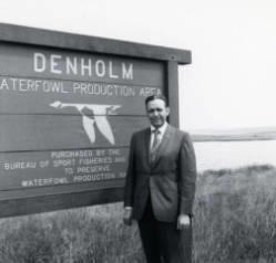 Frank Denholm standing by the Denholm Waterfowl Production Area sign