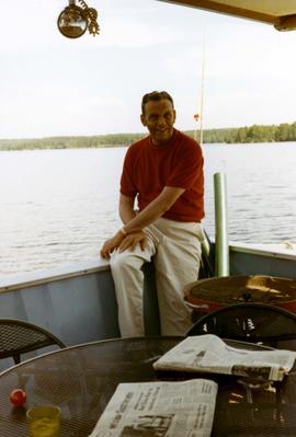 Frank Denholm relaxing on a houseboat on a lake or river.
