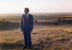 Congressman Frank Denholm standing in a pasture, there are cows in the background