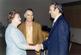 Frank Denholm is shaking hands with a women. A man is standing next to them.