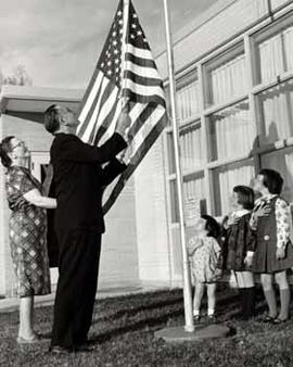 Representative Ben Reifel helps raise a US flag at an elementary school
