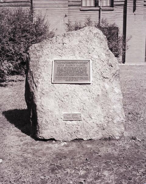 Monument dedicated to N.E. Hansen in recognition to his service to South Dakota State College, it was located in between the Administration Building and the Horticulture Building; the bronze citation reads: 'South Dakota State College seeks to perpetuate the memory of its long-time fruit and plant breeder: Niels Ebbesen Hansen. Born at Rebe, Denmark, January 4, 1866, came to the United States in 1873. Made Professor of Horticulture of South Dakota State College in 1895; Professor Emeritus in 1937. A world traveler and collector of plants, he developed drought resistant verities of fruits, flowers, and grasses for the Great Plains. His efforts provided the people of the Great Plains the means through which they enjoy a better living. August 25, 1959.' The rock was donated by Jno E. Gueffroy from near Colman, South Dakota. It is approximately 4.5 feet tall, 4.5 feet wide, with a 26 inch base.