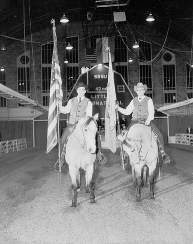 Two men on horseback are the color guard presenting the U.S. flag and the state of South Dakota flag the 1965 Little International Exposition at South Dakota State University.