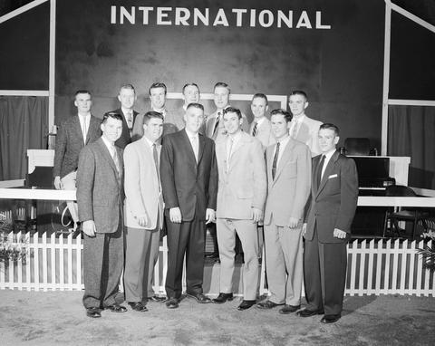 Group of men pose for a photograph in front of the false barn wall at the 1957 Little International Exposition at South Dakota State College.