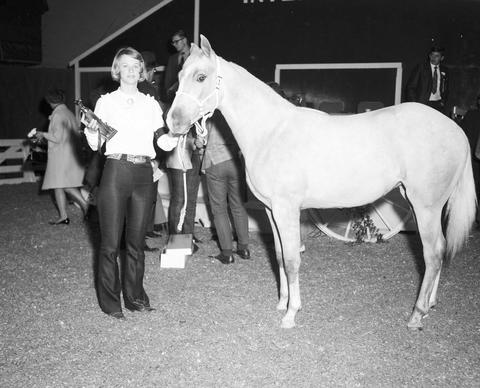 Woman holding a trophy stands in the arena by her prize winning horse at the 1970 Little International exposition at South Dakota State University.