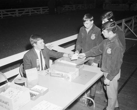 Future Farmers of America members stand in front of a table at the 1970 Little International exposition at South Dakota State University. A man sties behind the table with boxes of programs.