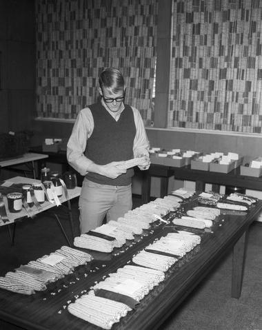Man looking at ears of corn in the agronomy exhibit at the 1969 Little International exposition at South Dakota. The are other seed samples on tables behind him.