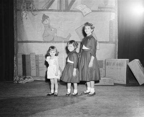 Three little girls wearing dresses stand on a stage for the Home Economics fashion show at the 1956 Little International Exposition at South Dakota State College.