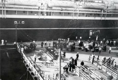 Passengers waiting to board a steamer ship by the dock at the port in Tokyo Bay at Yokahama, Japan, the ship is possibly a steamer ship called the Admiral from a line of ships owned and operated by the United States government; written in pencil on the back: Yokohama 1924.