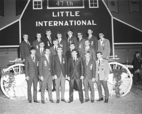 Group of men stand in front of the false barn wall at the 1970 Little International exposition at South Dakota State University.