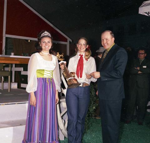 Little International Queen stands next to a woman holding a trophy and a man by the stage at the 1971 Little International exposition at South Dakota State University.