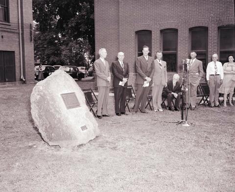 Unveiling of the rock and bronze tablet commemorating Dr. N.E. Hansen's work, it was located in between the Administration Building and the Horticulture Building; left to right: unknown man, Frank Cundill, South Dakota State College President Leinbach; Governor Mickelson; Dr. Hansen; Carl Hansen; Harry Dory; and Lucille Dory.