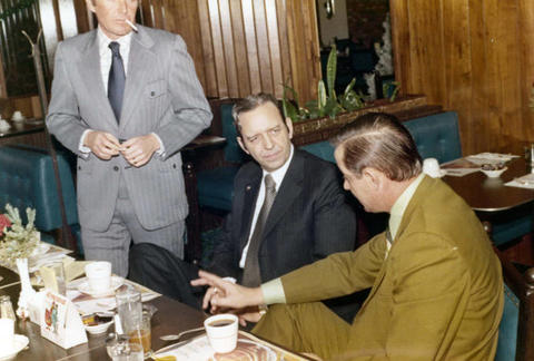 Frank Denholm and Richard Kneip are having a discussion in a restaurant with another man.