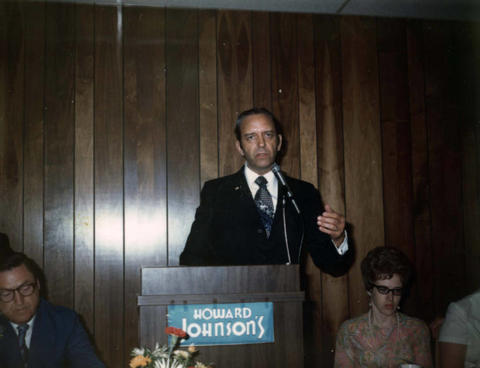 Frank Denholm speaking at an event in a Howard Johnson's convention center.