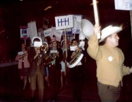 Campaign rally for the South Dakota Democratic Party. There is a parade of people, some are holding campaign signs and other are playing musical instruments in a band.
