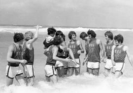 South Dakota basketball delegation to Cuba players in USA team uniforms standing in the surf on Cuban beach. One player is holding a woman.