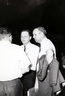 Frank Denholm at the South Dakota Democratic Party convention in Huron, South Dakota. He is holding his coat jacket under his arm and talking with Peder Ecker and another man.