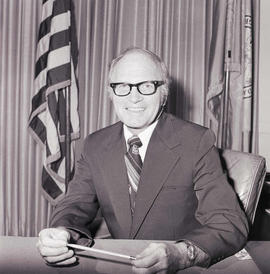 South Dakota State University President Sherwood O. Berg sitting at a desk in his office in the Administration building