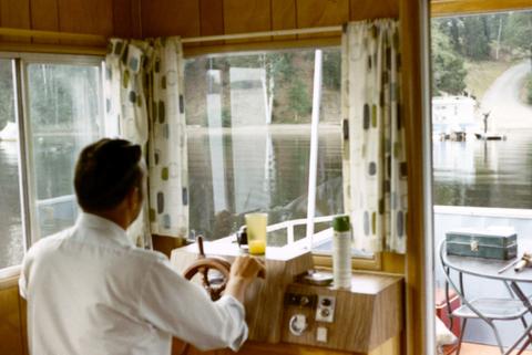 Frank Denholm steering a house boat on a lake.