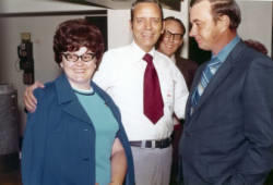 Frank Denholm standing with two constituents at a campaign event. His hands is on the woman's shoulders.