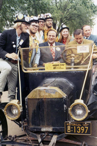 Jam Abourezk and Dick Kneip are seated in the bummobile with the Hobo Day committee at South Dakota State University in Brookings, South Dakota.