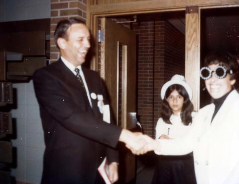 Frank Denholm shaking the hand of a woman who is wearing glasses. A a younger woman is standing in the doorway.