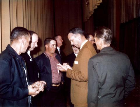 Frank Denholm signing an autograph. There is a group of men standing around him.