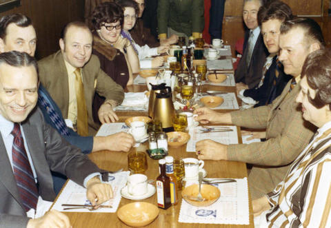 Frank Denholm seated at a long table with a group of people in a restaurant.