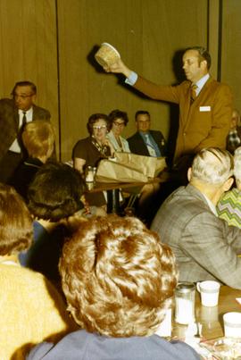 Frank Denholm at a campaign event. He is holding a bowl while the audience is seated on chairs around him.